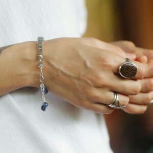 Close-up of hands wearing silver jewelry, showing rings and a bracelet on an arm with tattoos