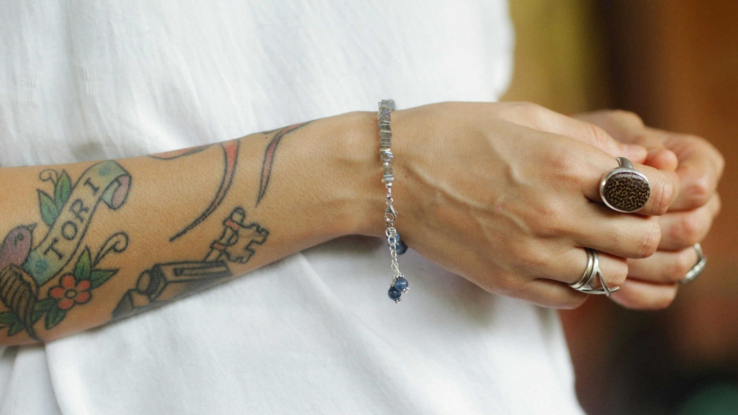 Close-up of hands wearing silver jewelry, showing rings and a bracelet on an arm with tattoos